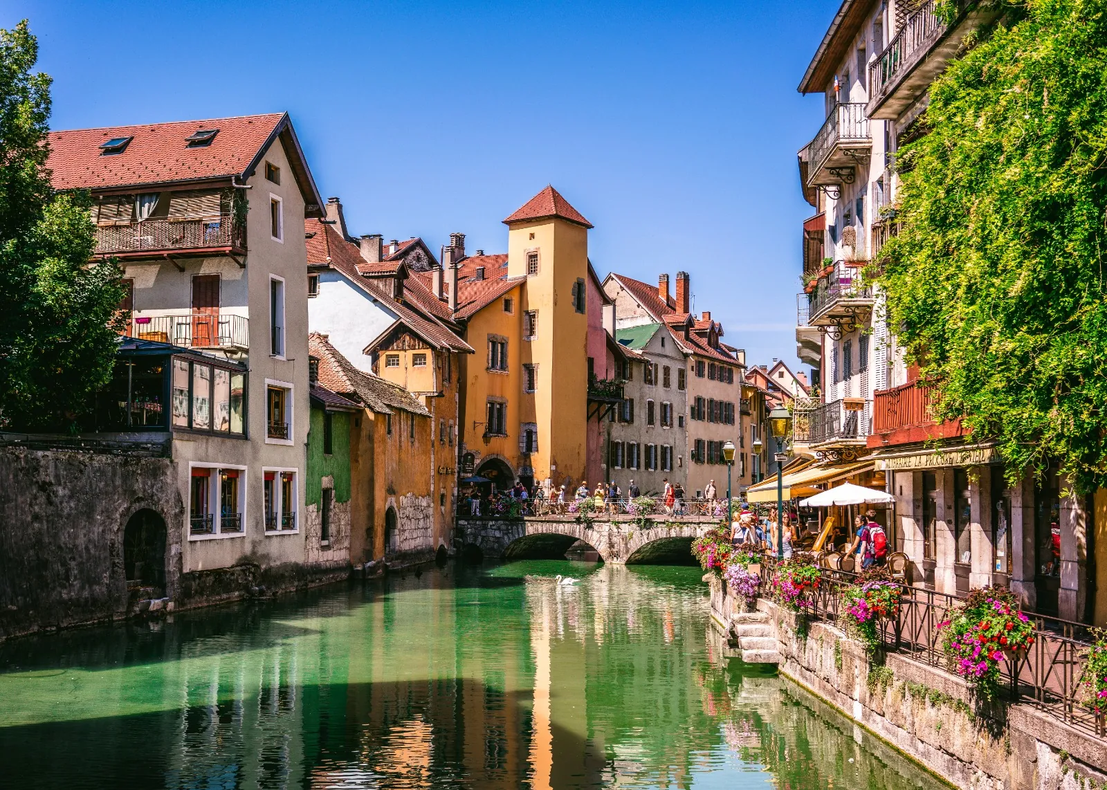 Narrow cobbled lane in medieval Annecy with pastel stone façades, arched passages and geraniums